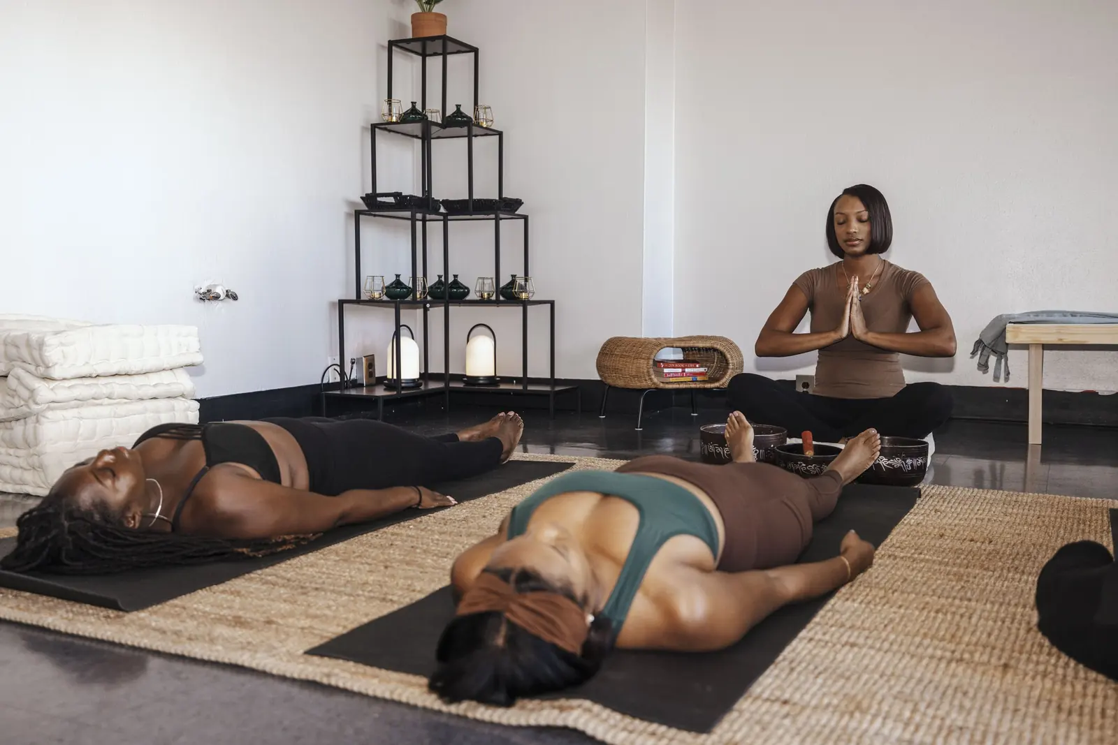 Kalish Nesbitt sitting with hands at her chest while two people rest on mats during a Calm and Co. session