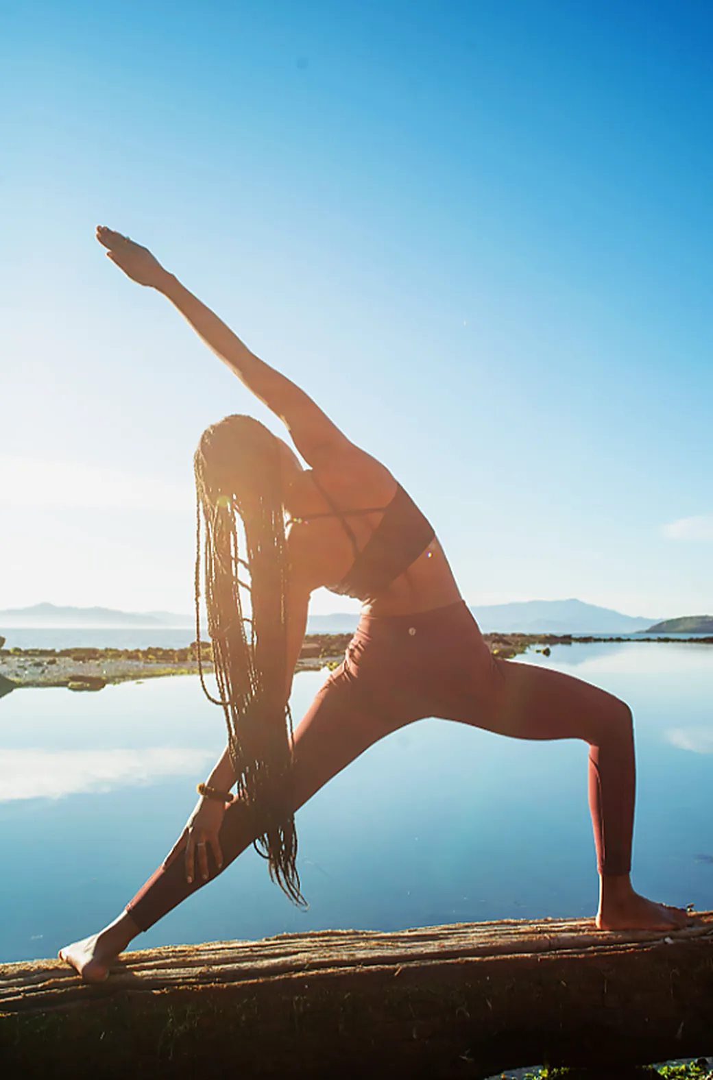 A woman holding an extended side angle pose on a wooden dock beside still water